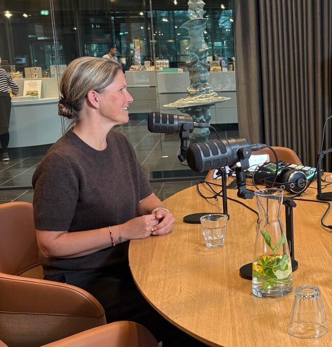 Annelou van Noort aan tafel met microfoons tijdens een podcastopname